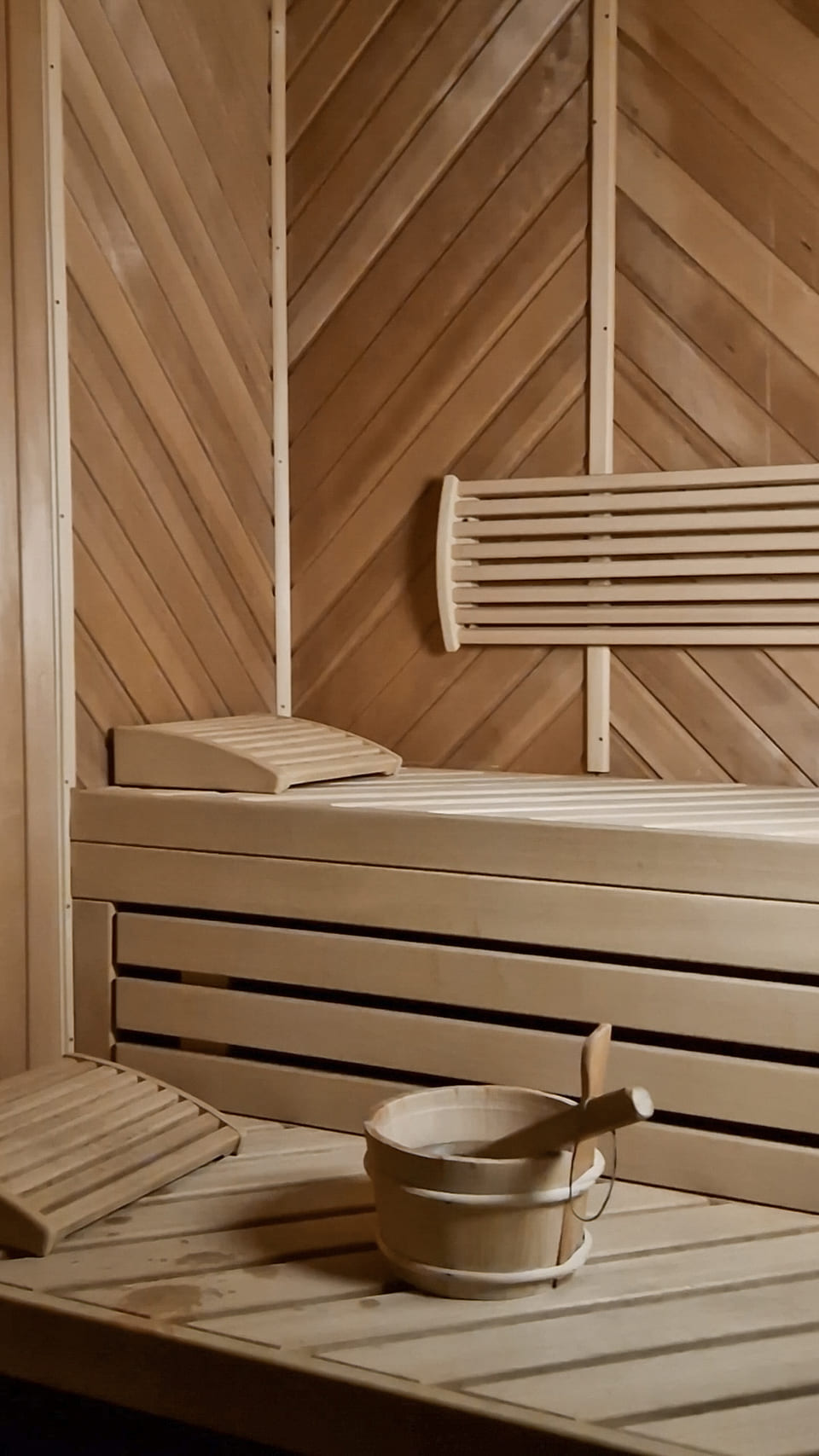 Blick in die finnische Sauna mit hellen Holzbänken und Aufgusskübel